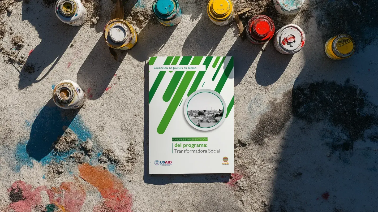 Portada del manual de Transformadora Social sobre una mesa con botes de pintura en aerosol