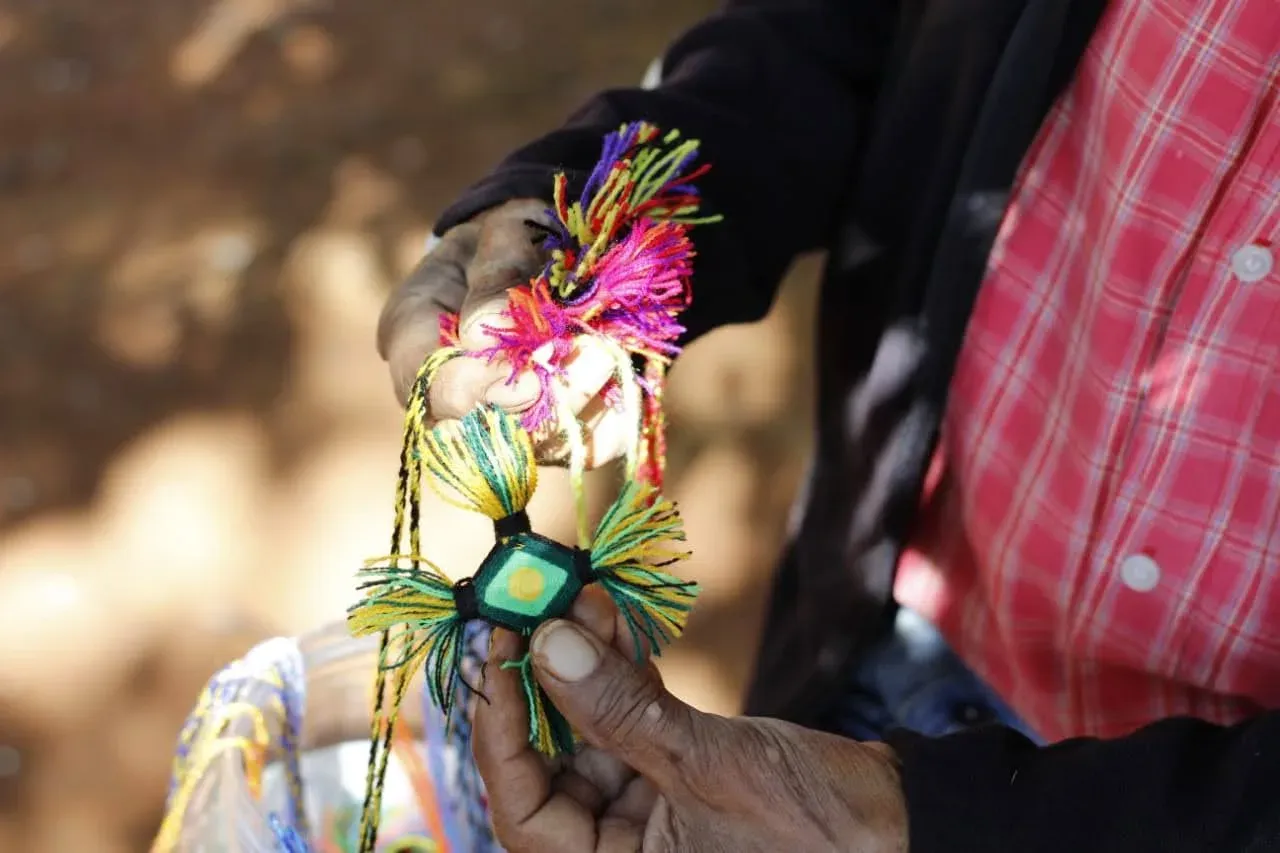Manos sostienen una figura tejida con estambres de colores en el taller de la escuela